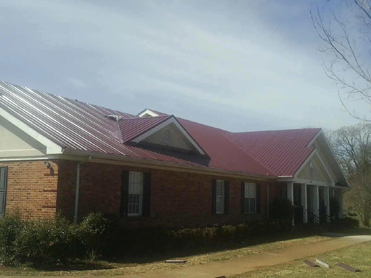 Red metal roof with gabled entries on a long brick building, from a Hail Damage Roof Repair job in Gleneden Beach