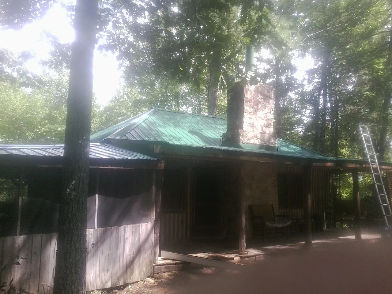 Green metal roof and stone chimney above a log cabin porch in Gleneden Beach