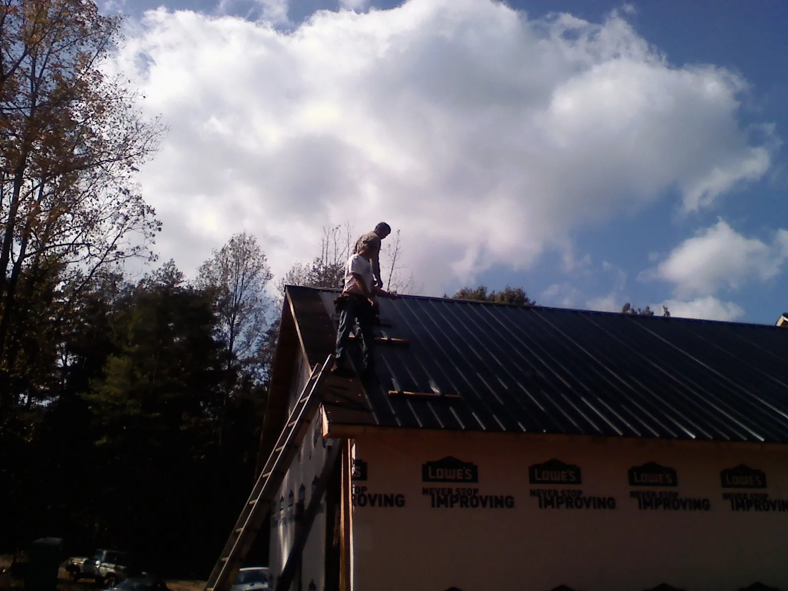 Roofer fastening dark metal panels high against a cloudy sky, from a Roof Inspection job in Gleneden Beach