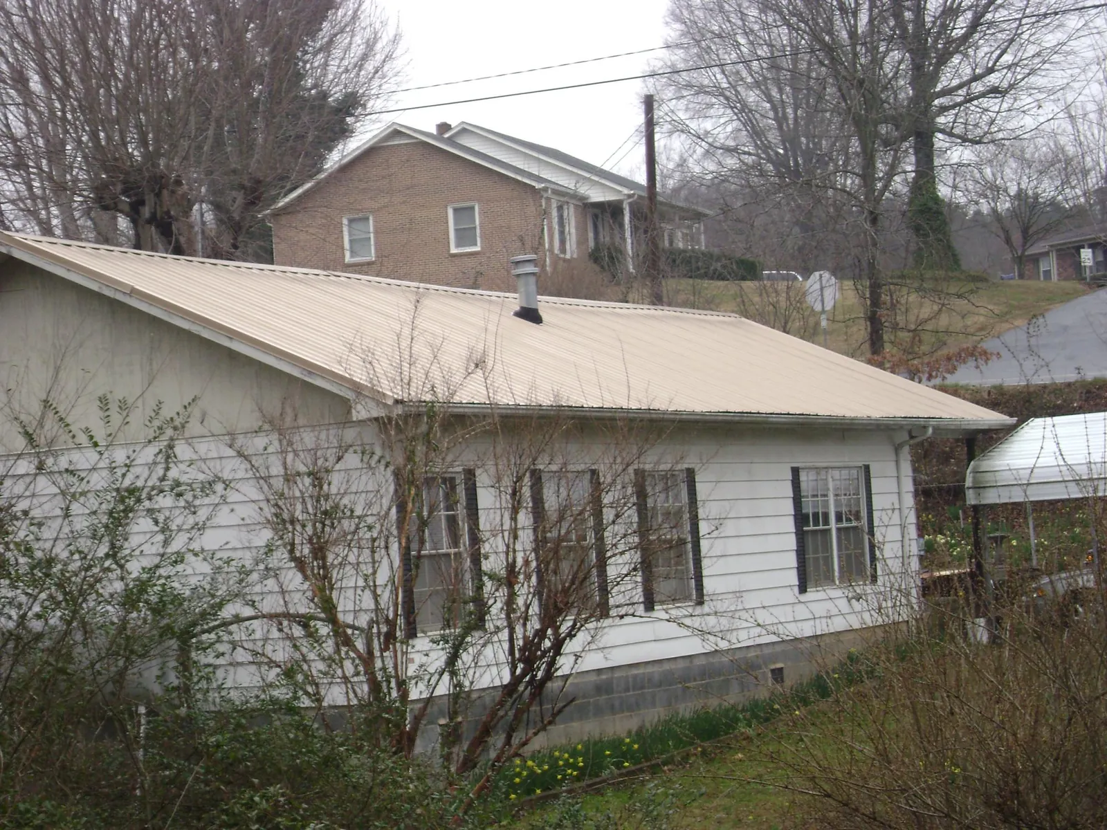 Tan metal roof on a white sided house set into a hillside — Commercial Roofing by Roofing Brothers in Gleneden Beach